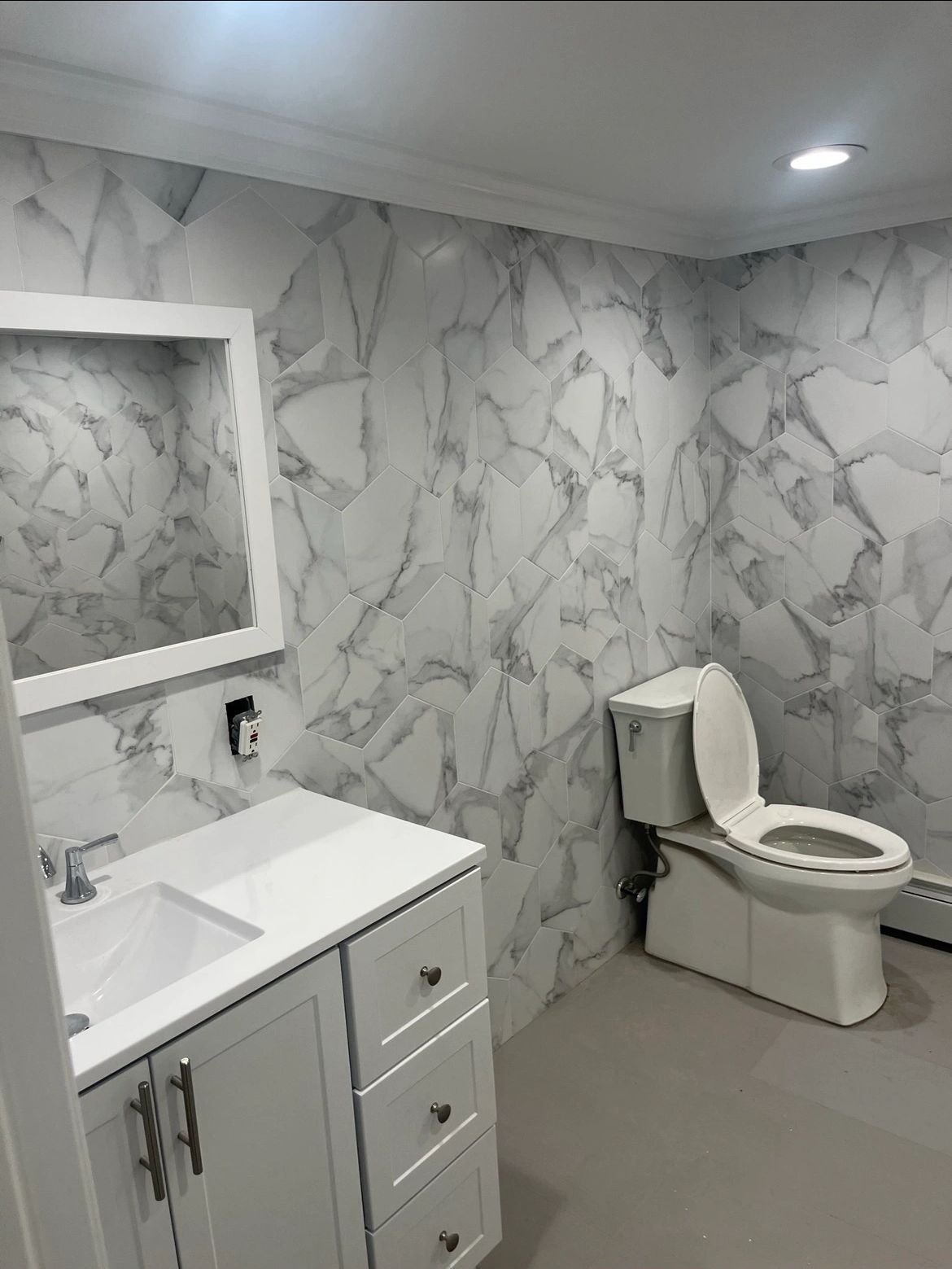A bathroom with a toilet , sink , mirror and marble walls.