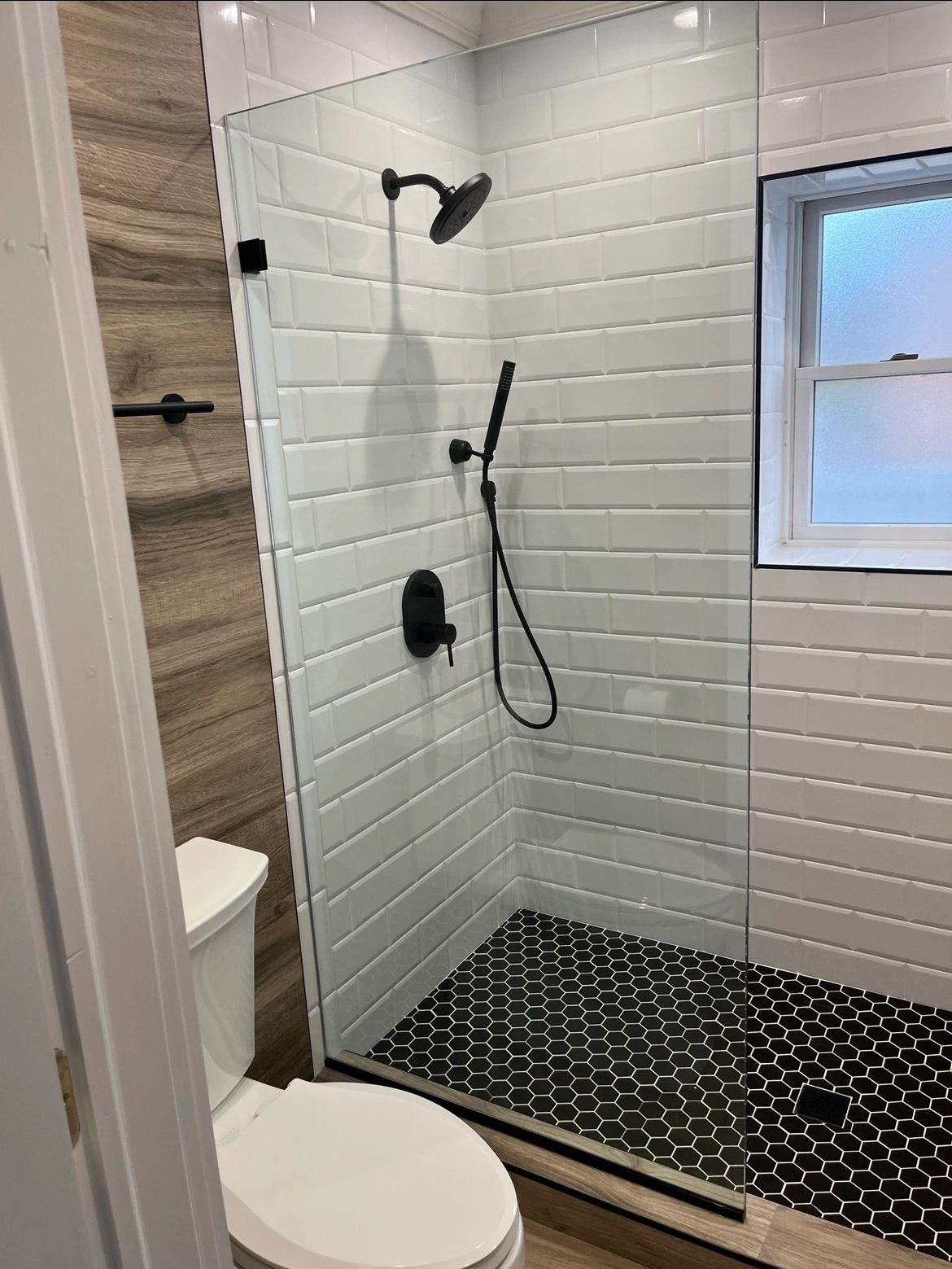 A bathroom with a walk in shower , toilet and window.