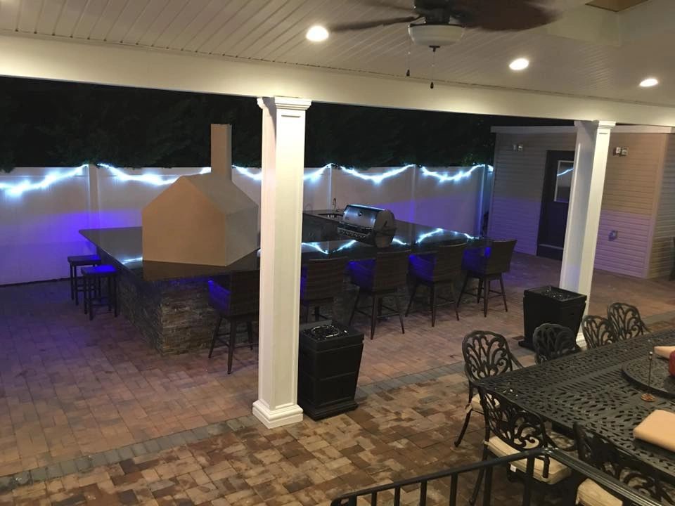 A patio with a table and chairs and a grill at night.