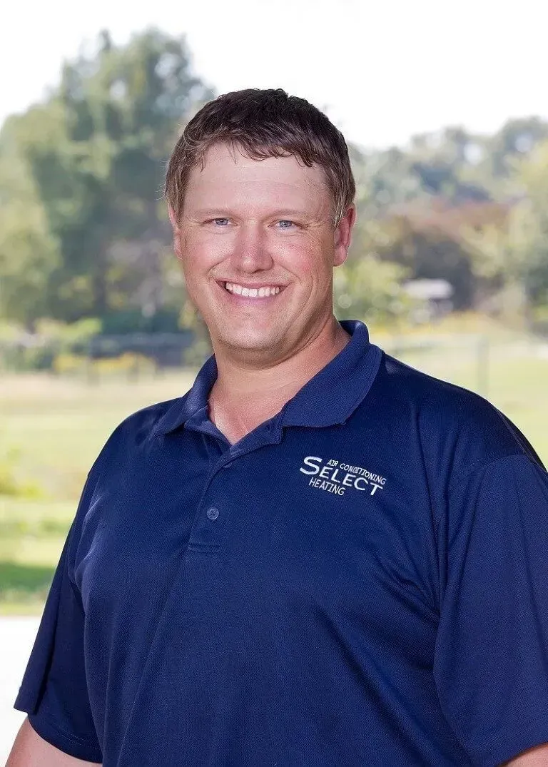 Man smiling, wearing a blue polo shirt with a logo, set outdoors with trees in the background.