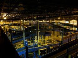 A large warehouse filled with lots of conveyor belts and stairs at night.