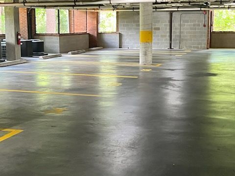 Empty parking garage with a gray concrete floor, columns, and yellow parking space markings.
