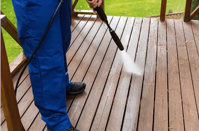 A person is cleaning a wooden deck with a high pressure washer.