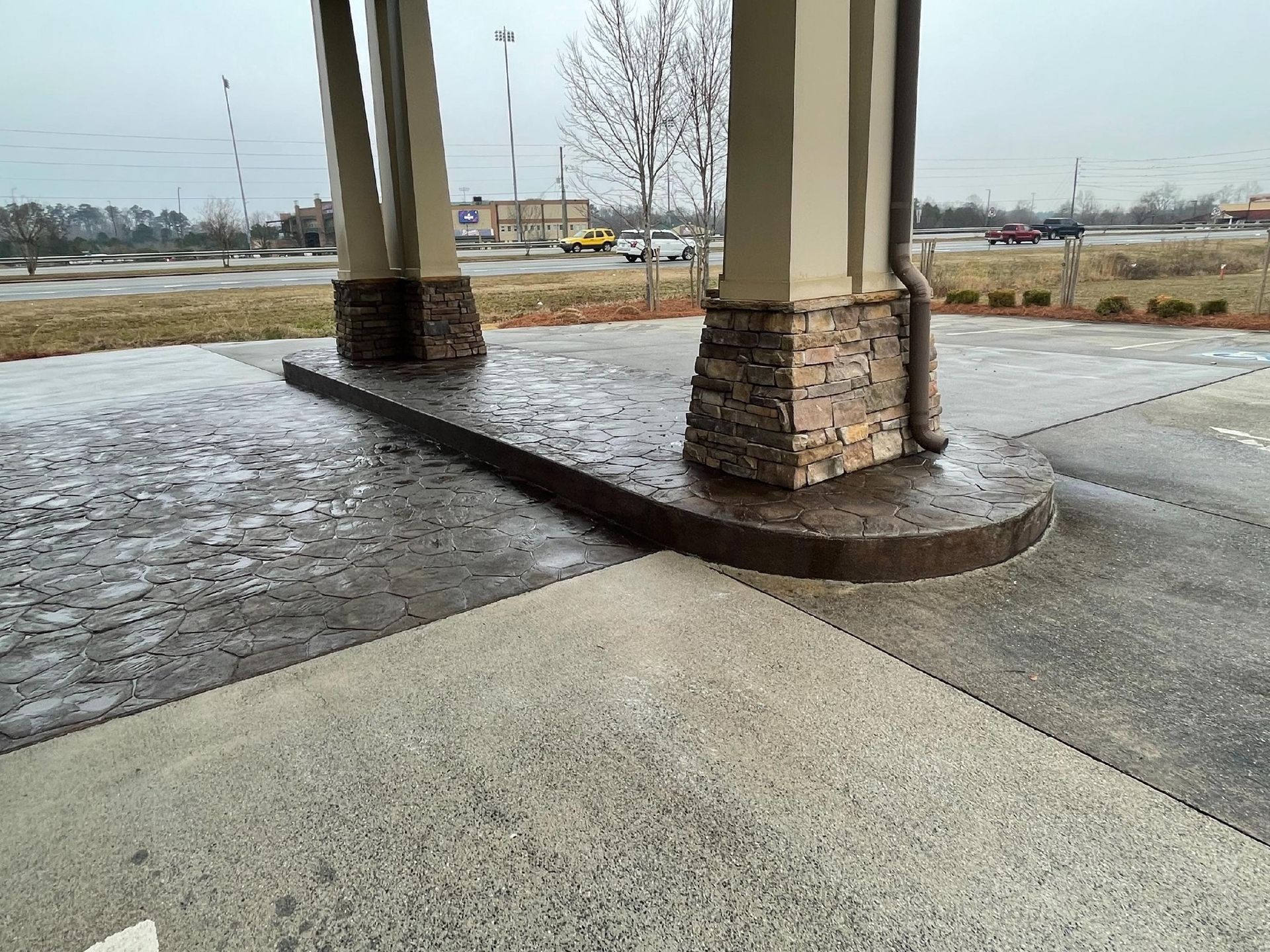 Concrete pillars with stone bases on a curved concrete walkway, exterior view.
