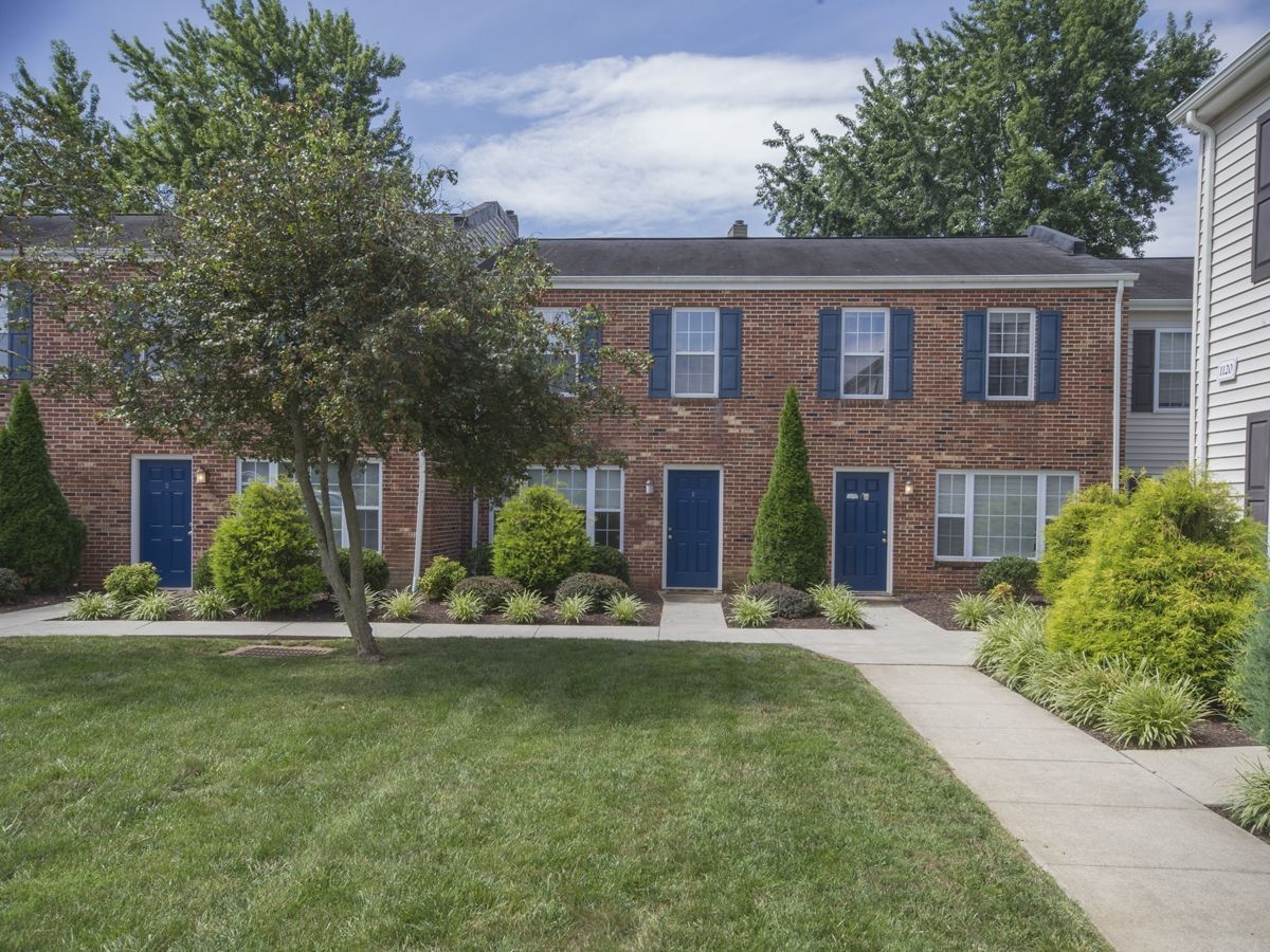 A brick apartment building with blue shutters and a lush green lawn.