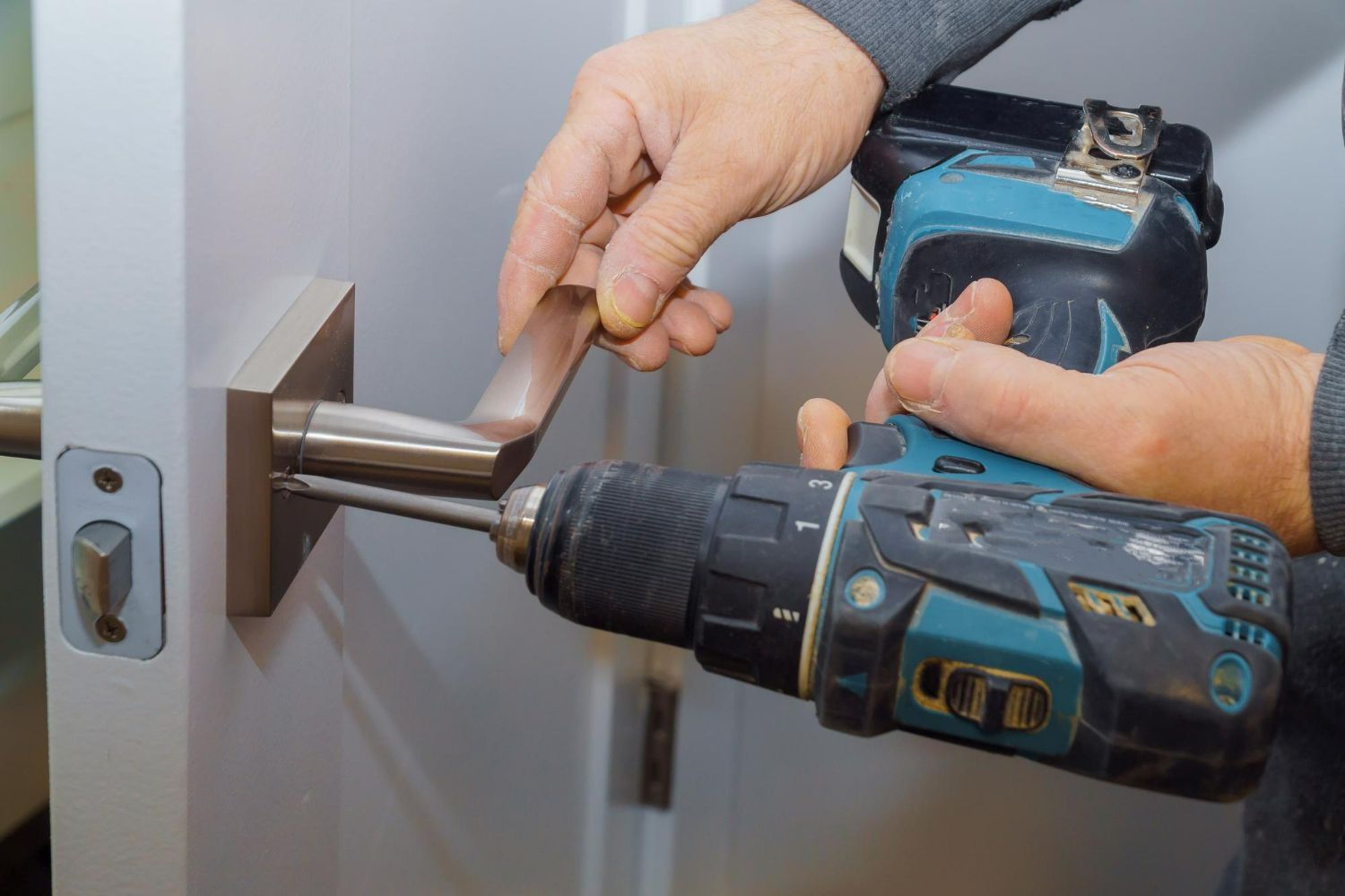 A man is using a drill to fix a door handle.