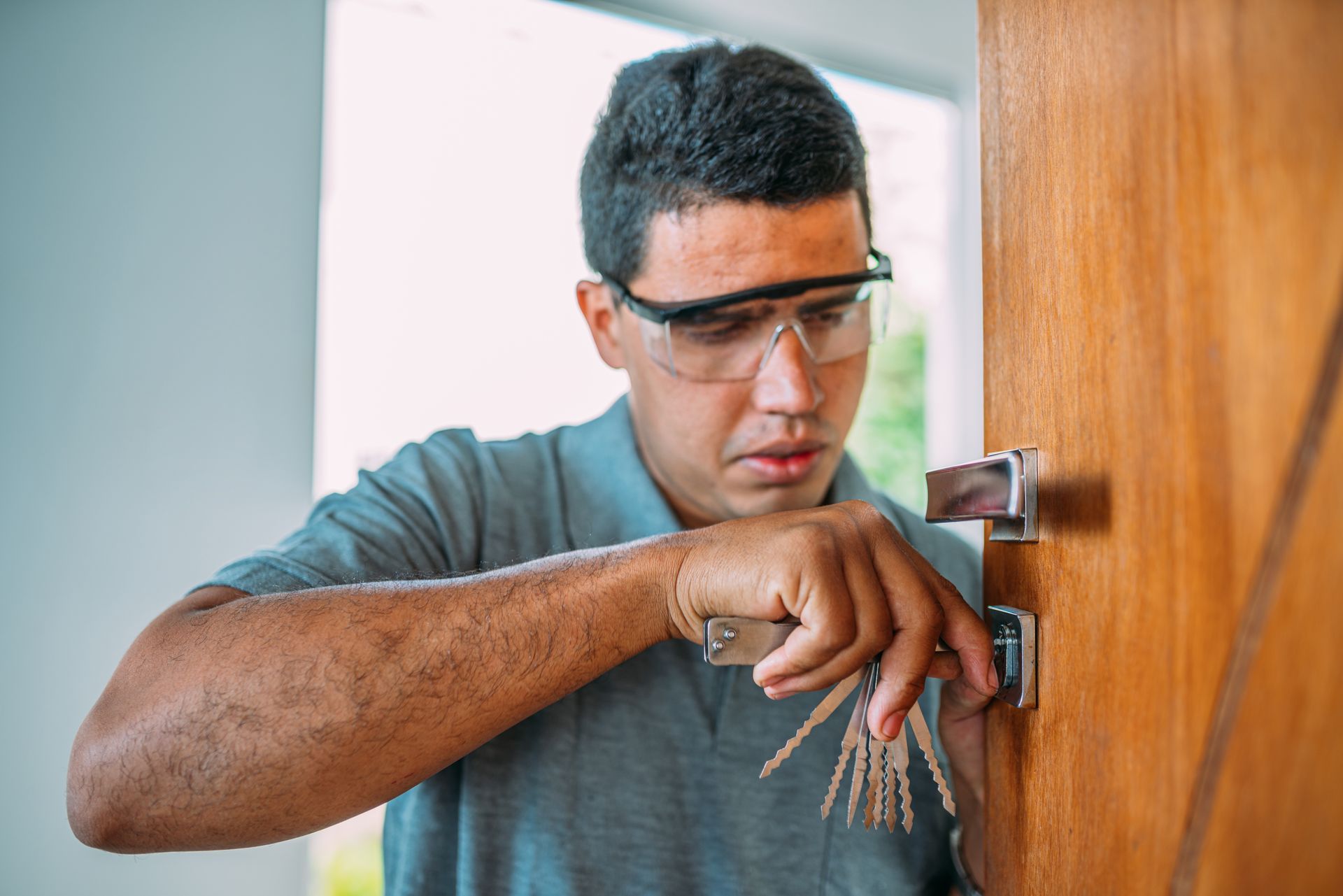 Man with safety glasses rekeying a lock on a wooden door.