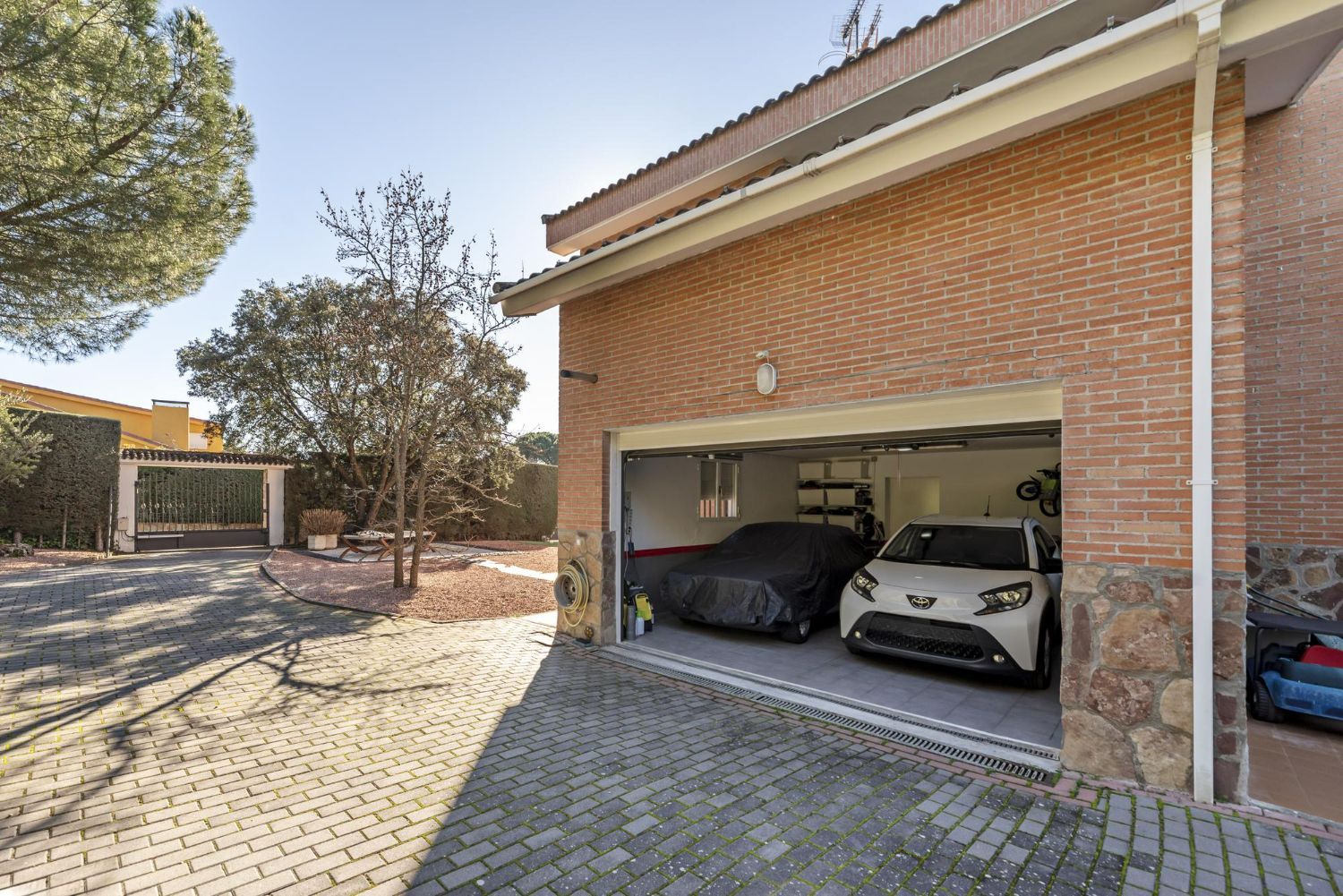 Two cars are parked in a garage with the door open.