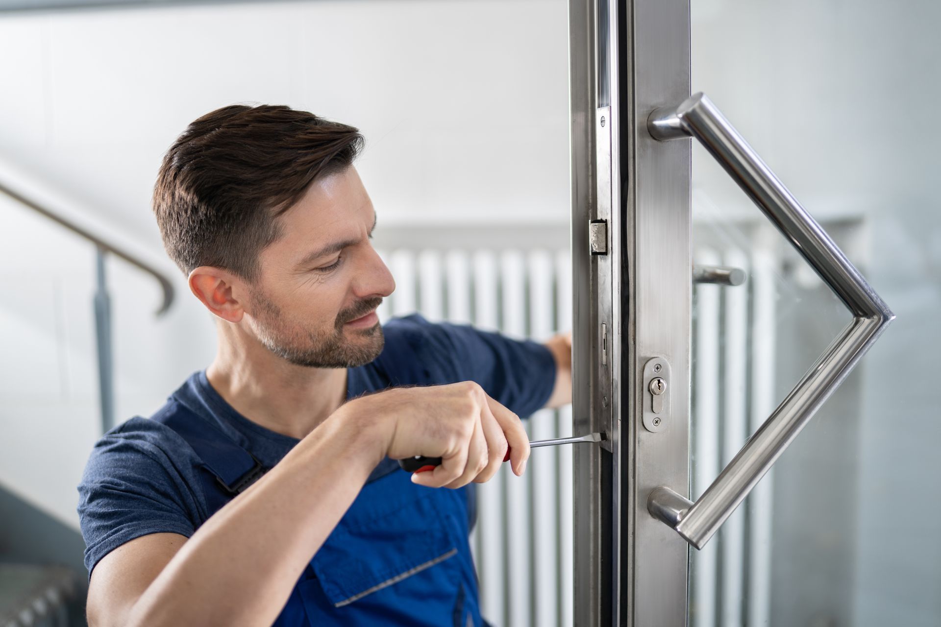Locksmith in blue uniform repairing a door lock with a screwdriver.