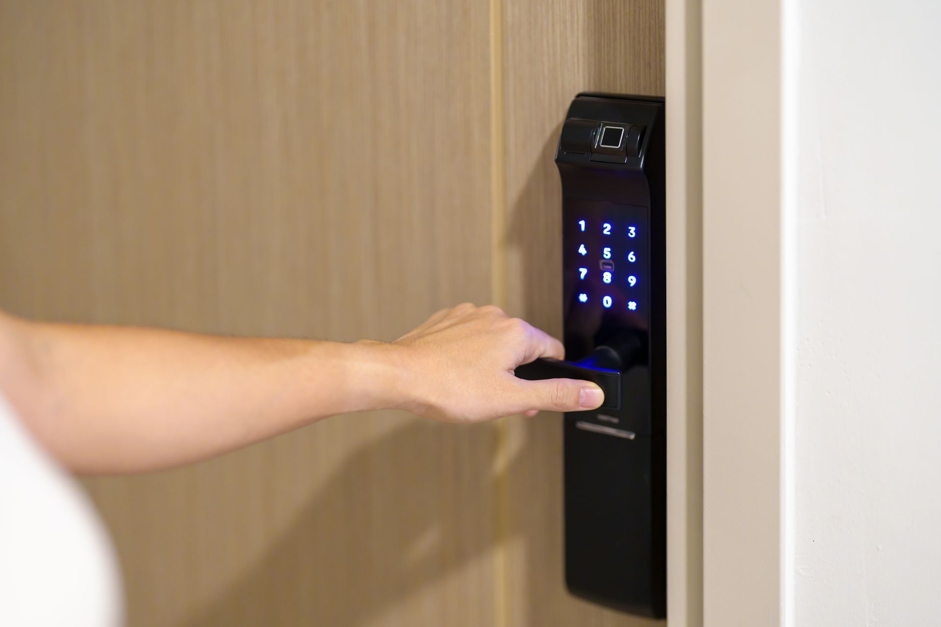 Hand unlocking a black smart door lock with fingerprint scanner.