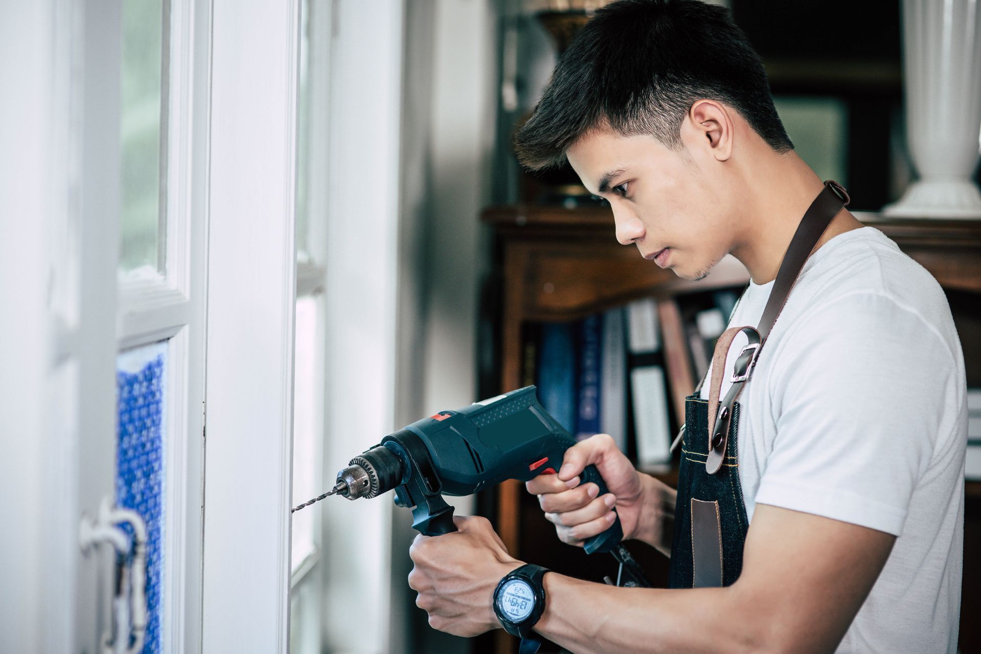 A man is using a drill to fix a window.