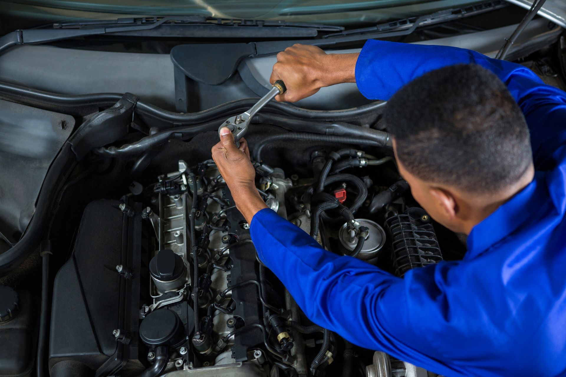 A man is working on the engine of a car with a wrench.