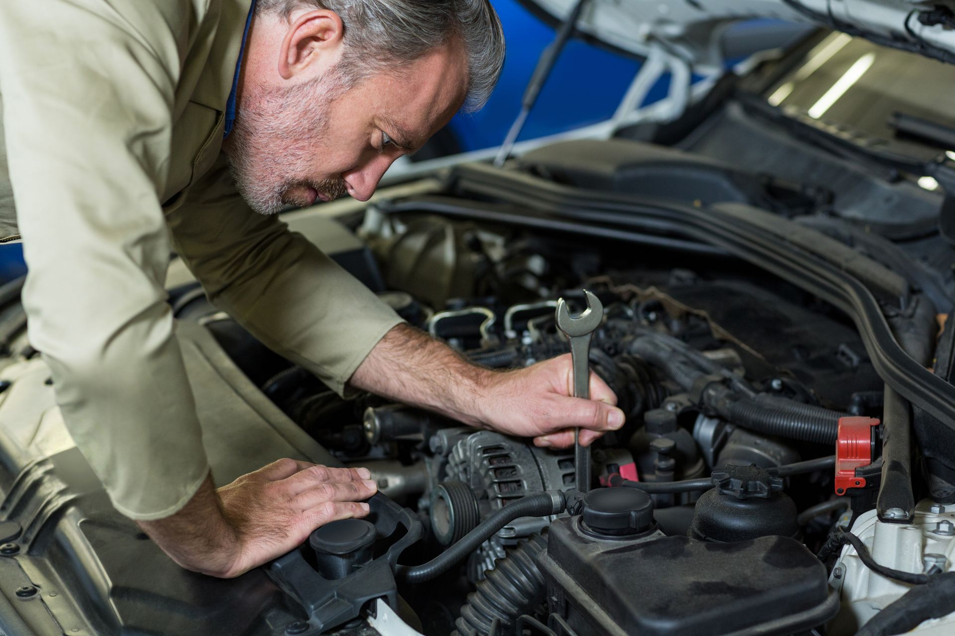 A man is working on the engine of a car with a wrench.