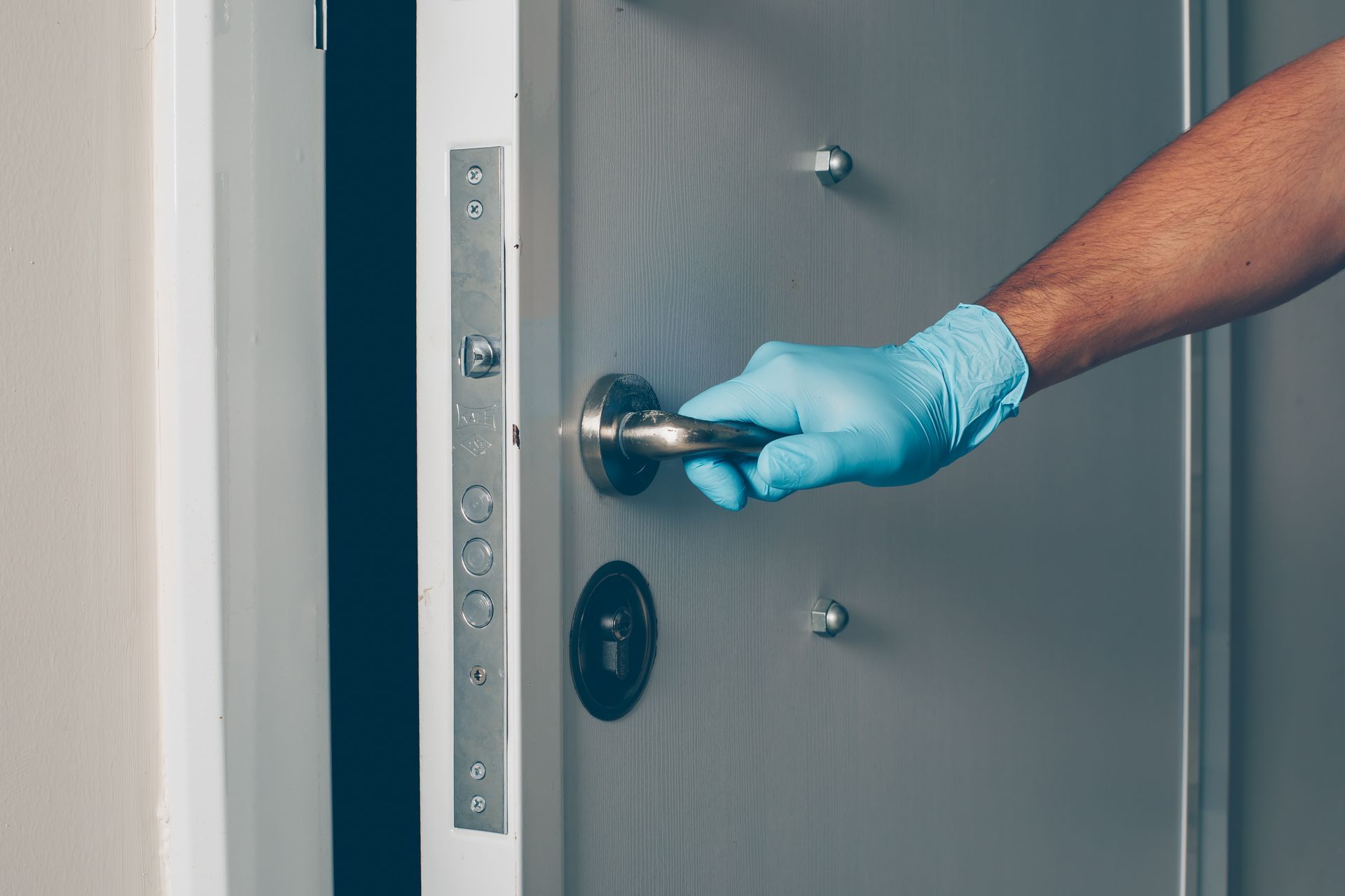 A person wearing blue gloves is opening a door.