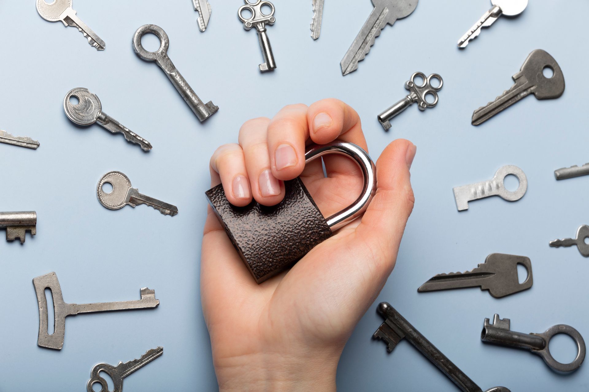 A person is holding a padlock in their hand surrounded by keys.