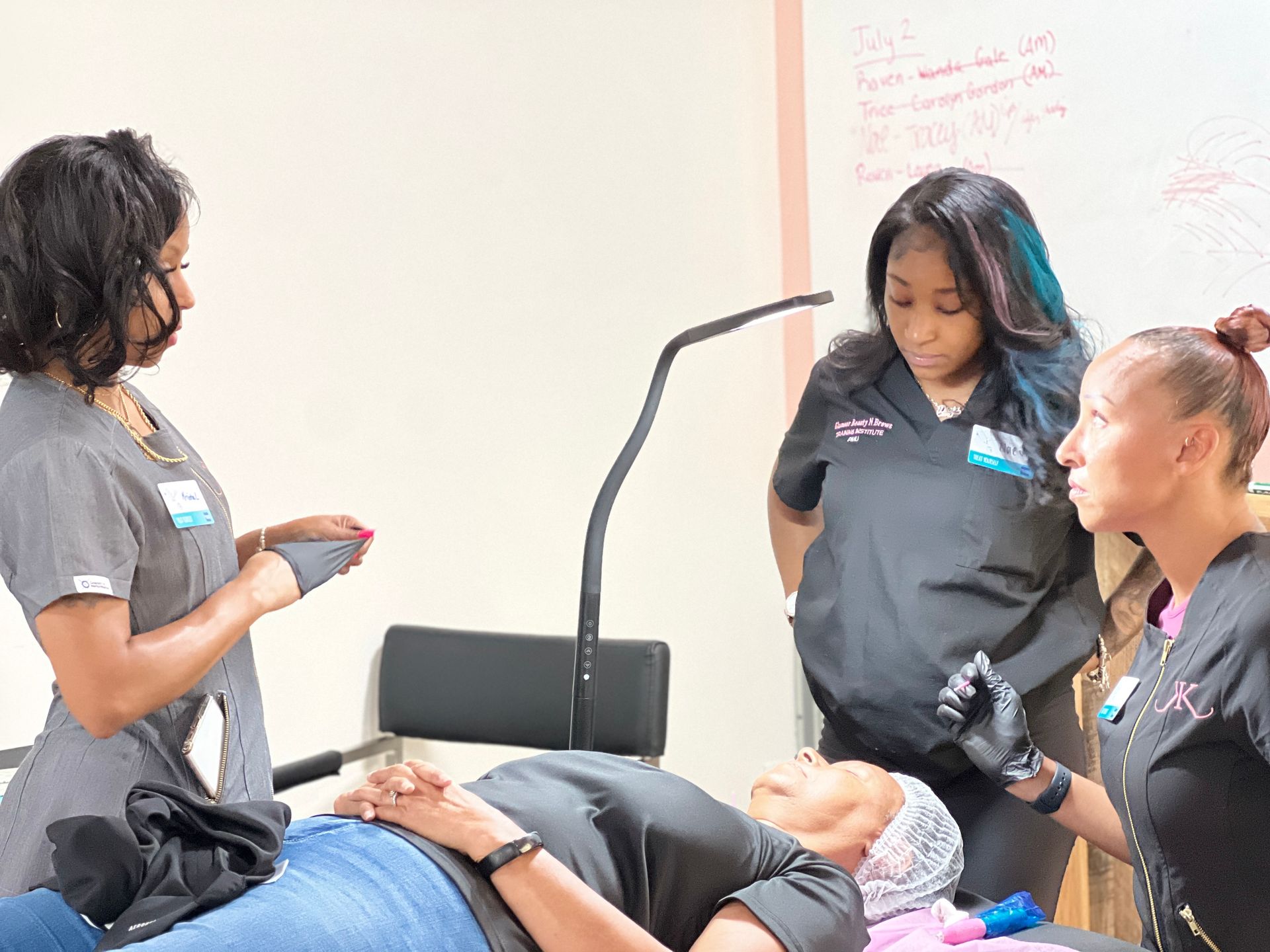 A group of women are standing around a woman laying on a bed.