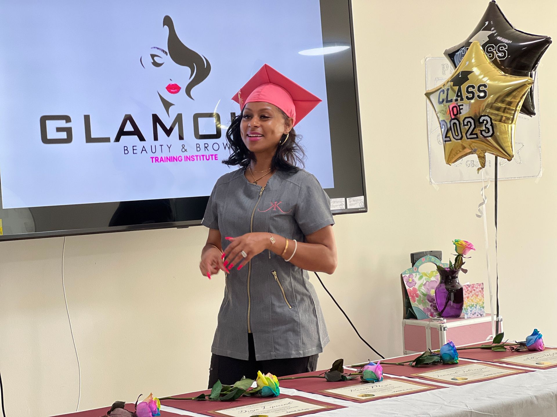 A woman in a graduation cap and gown is standing in front of a table.