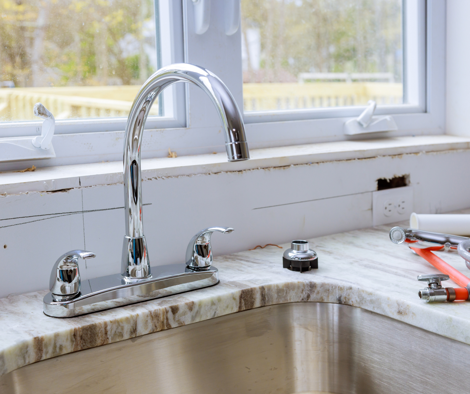 Kitchen sink with chrome faucet installed on marble countertop, tools nearby.