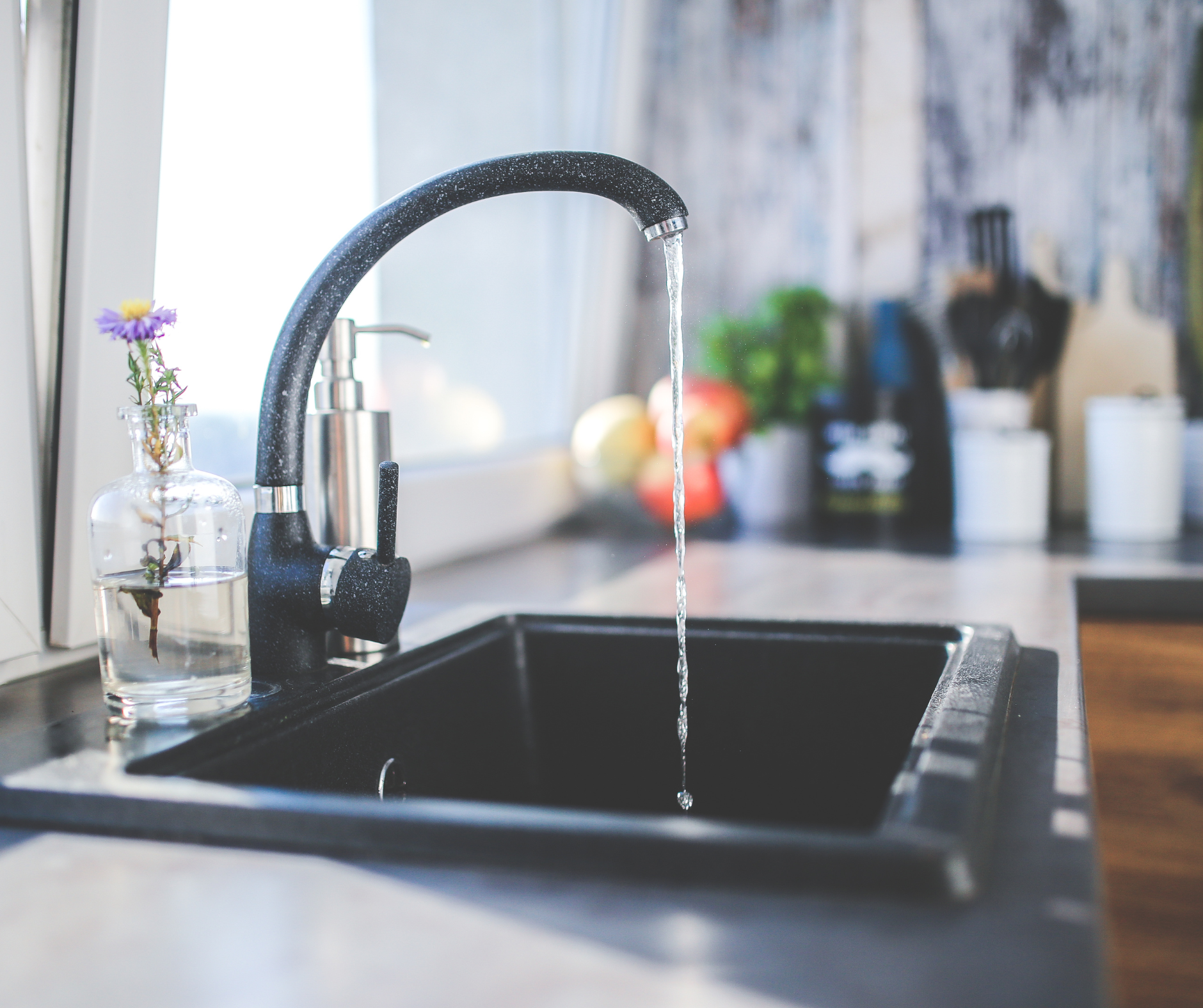 Black kitchen sink with running water from a curved faucet; flowers in a glass vase sit nearby.