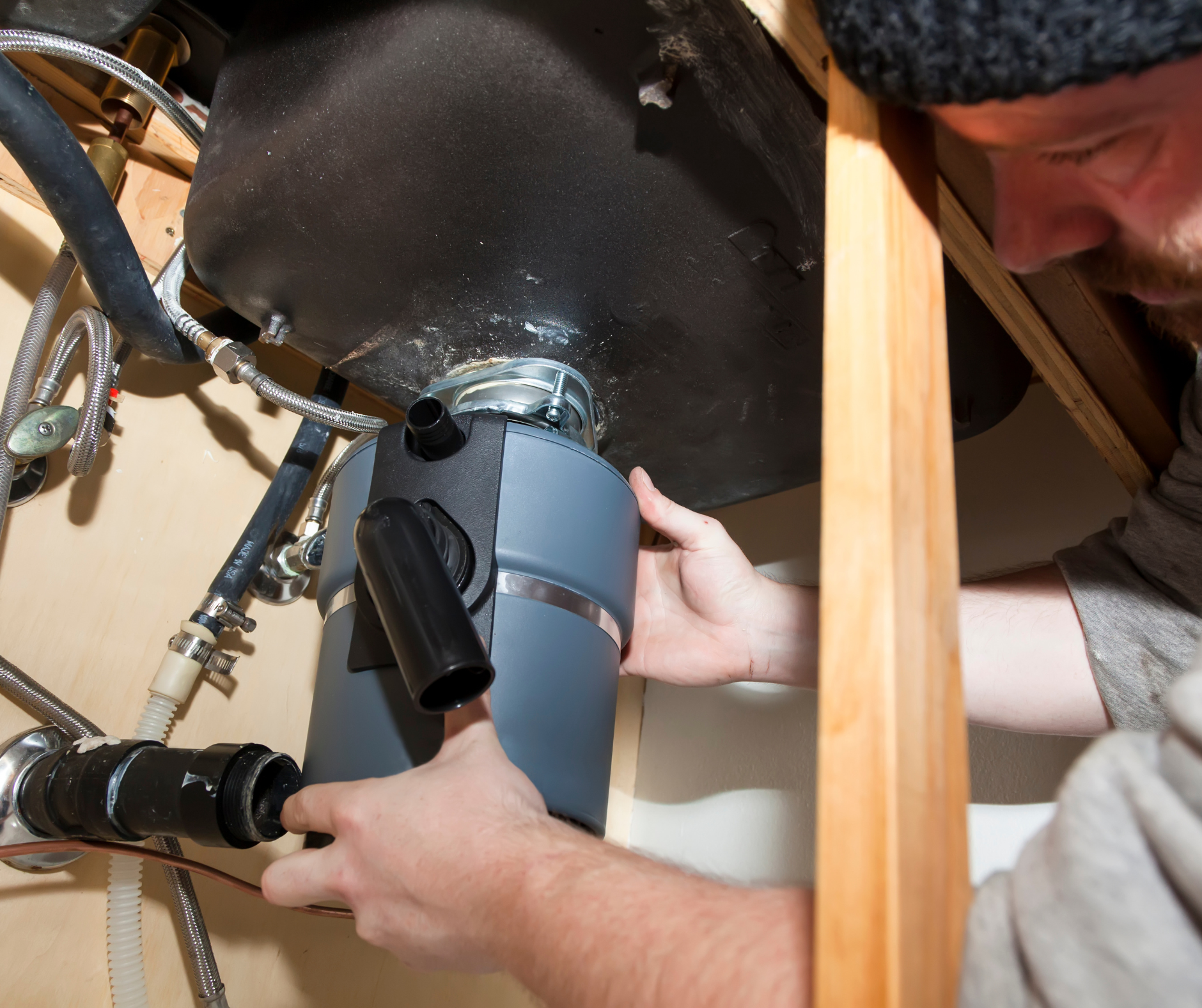 Person installing a garbage disposal under a kitchen sink.