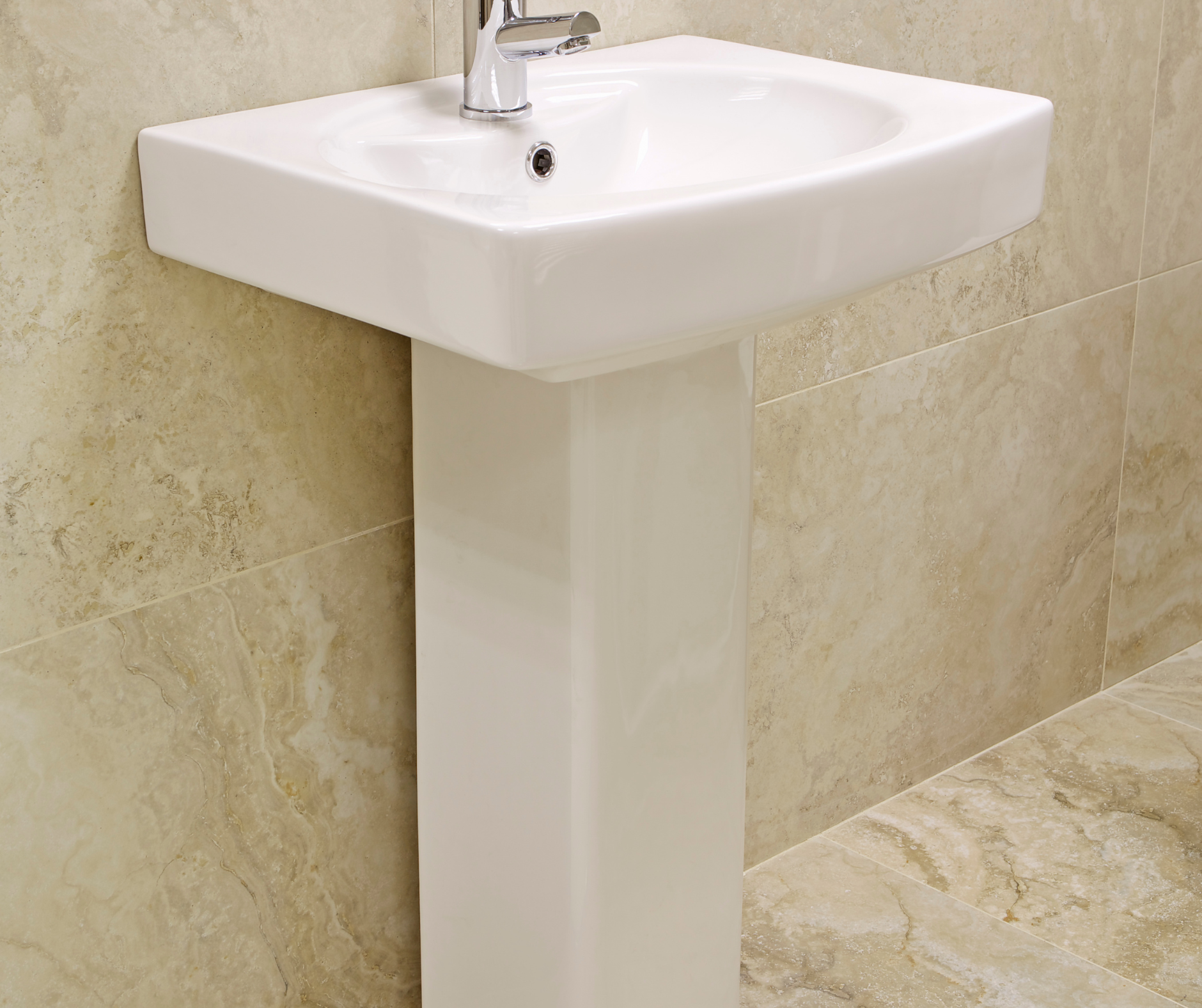 White pedestal sink in bathroom with beige tile walls.