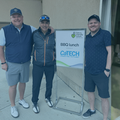 Three men smile next to a sign 