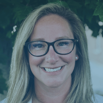 A smiling person with long blonde hair and dark-rimmed glasses