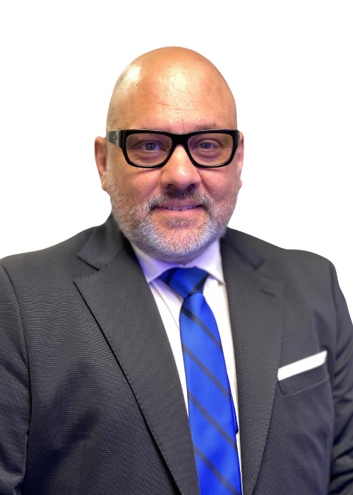A man with a bald head and beard wearing glasses, a suit, and a blue tie.