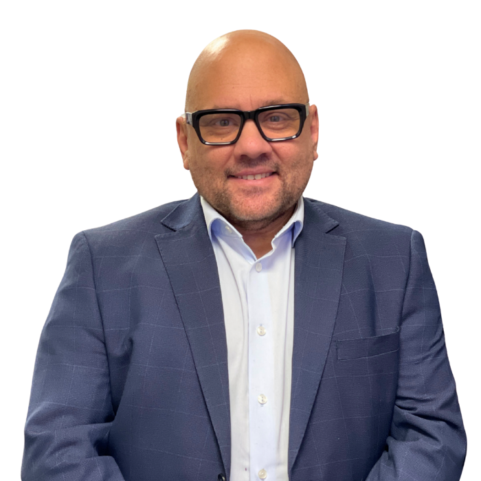 Man in a black suit smiling, white shirt open at the collar, pocket square.