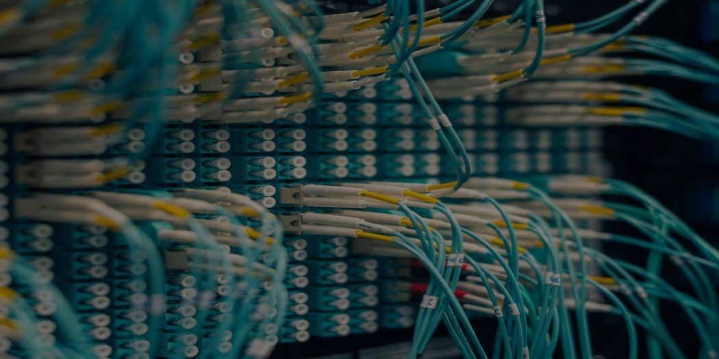 Close-up of a server room, with rows of connected cables, in shades of teal and yellow.