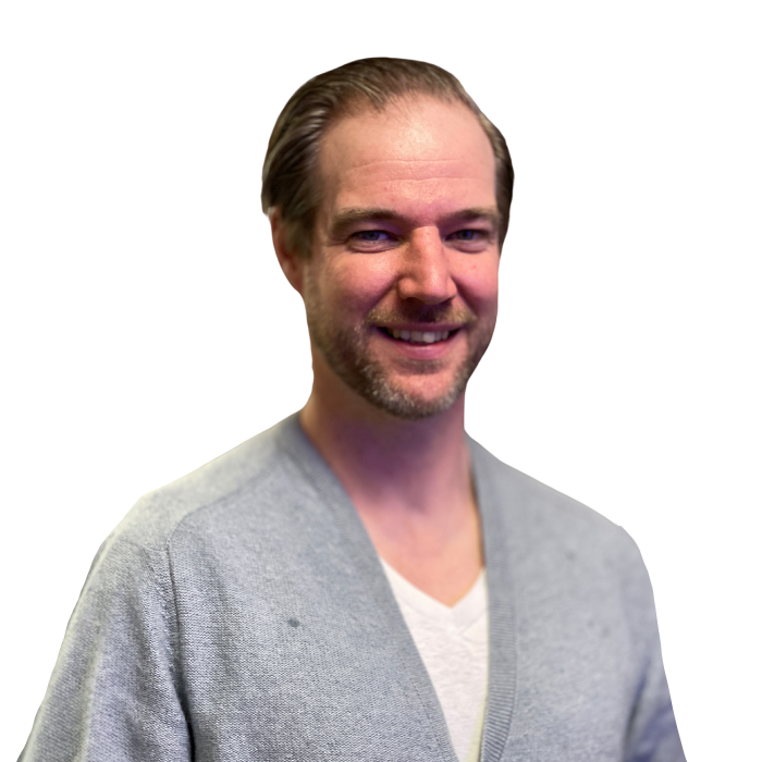 Man smiling, light skin, blue-gray sweater, white undershirt, light stubble, against a white background.