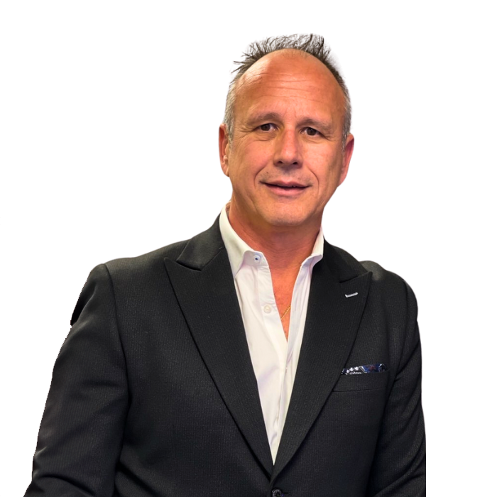 Man in a black suit smiling, white shirt open at the collar, pocket square.