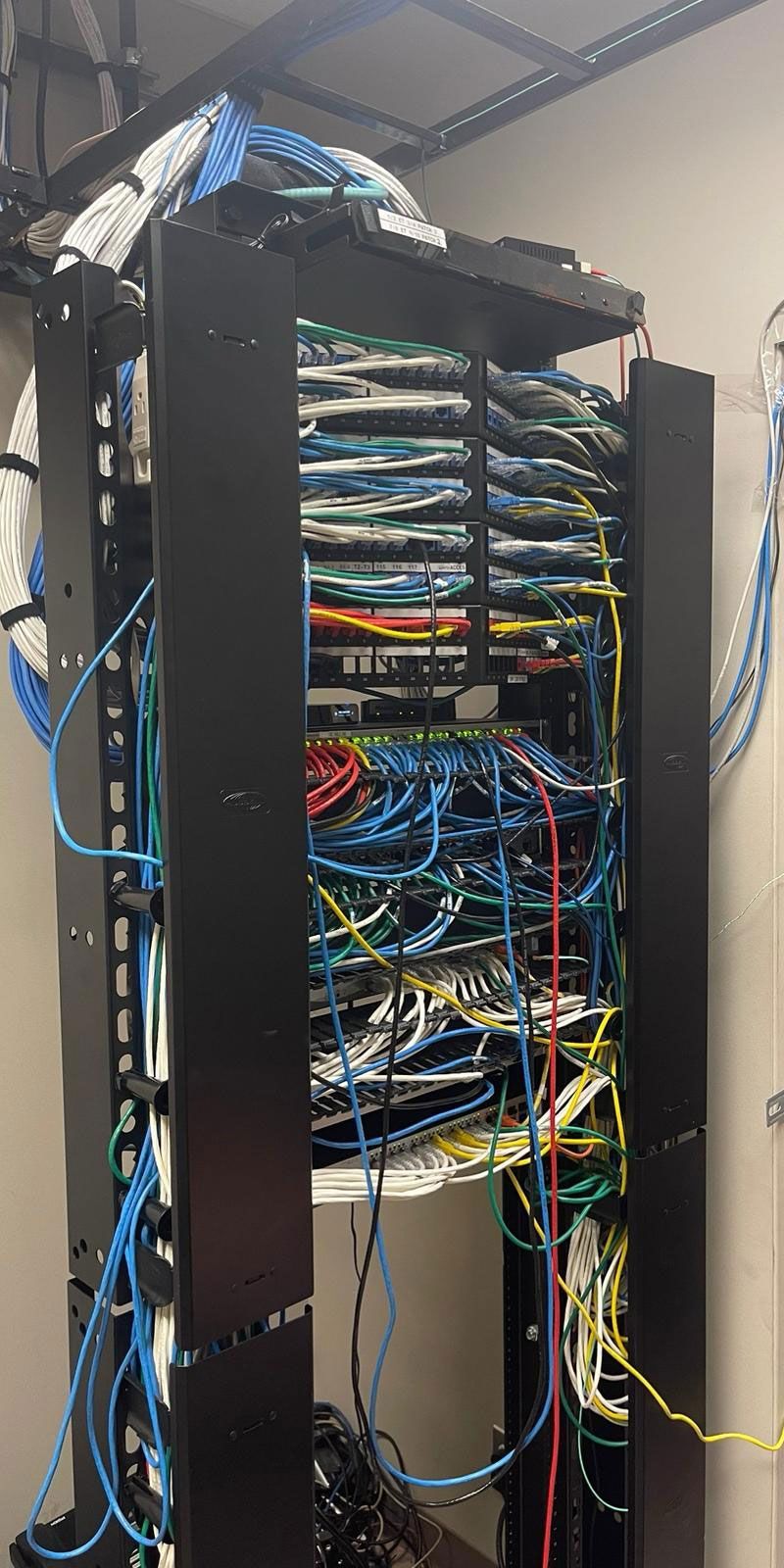 A black server rack filled with tangled network cables of various colors, mounted against a wall.