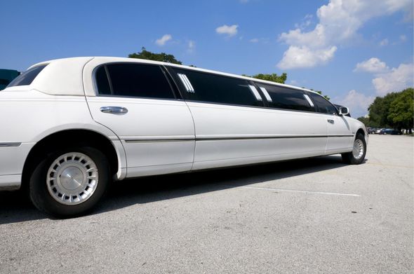 White stretch limousine parked on a paved road under a blue sky