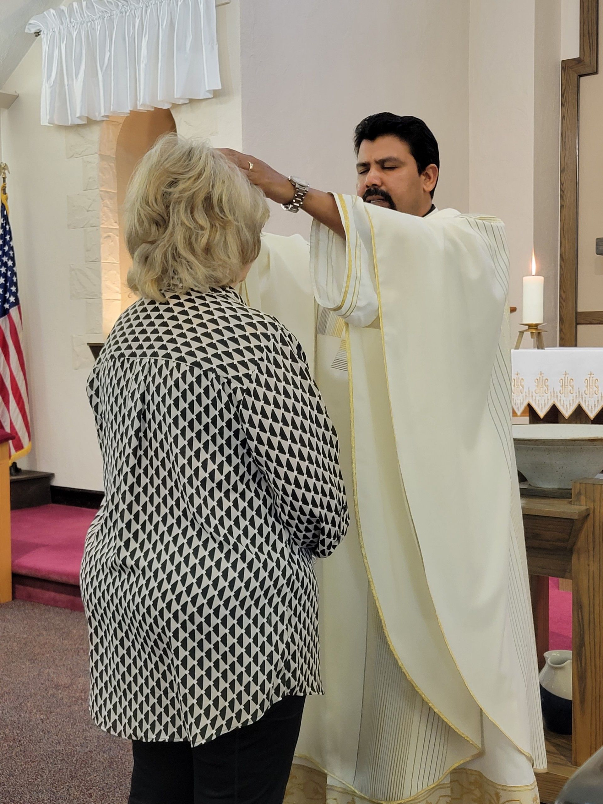 A man in a white robe is blessing a woman in a church
