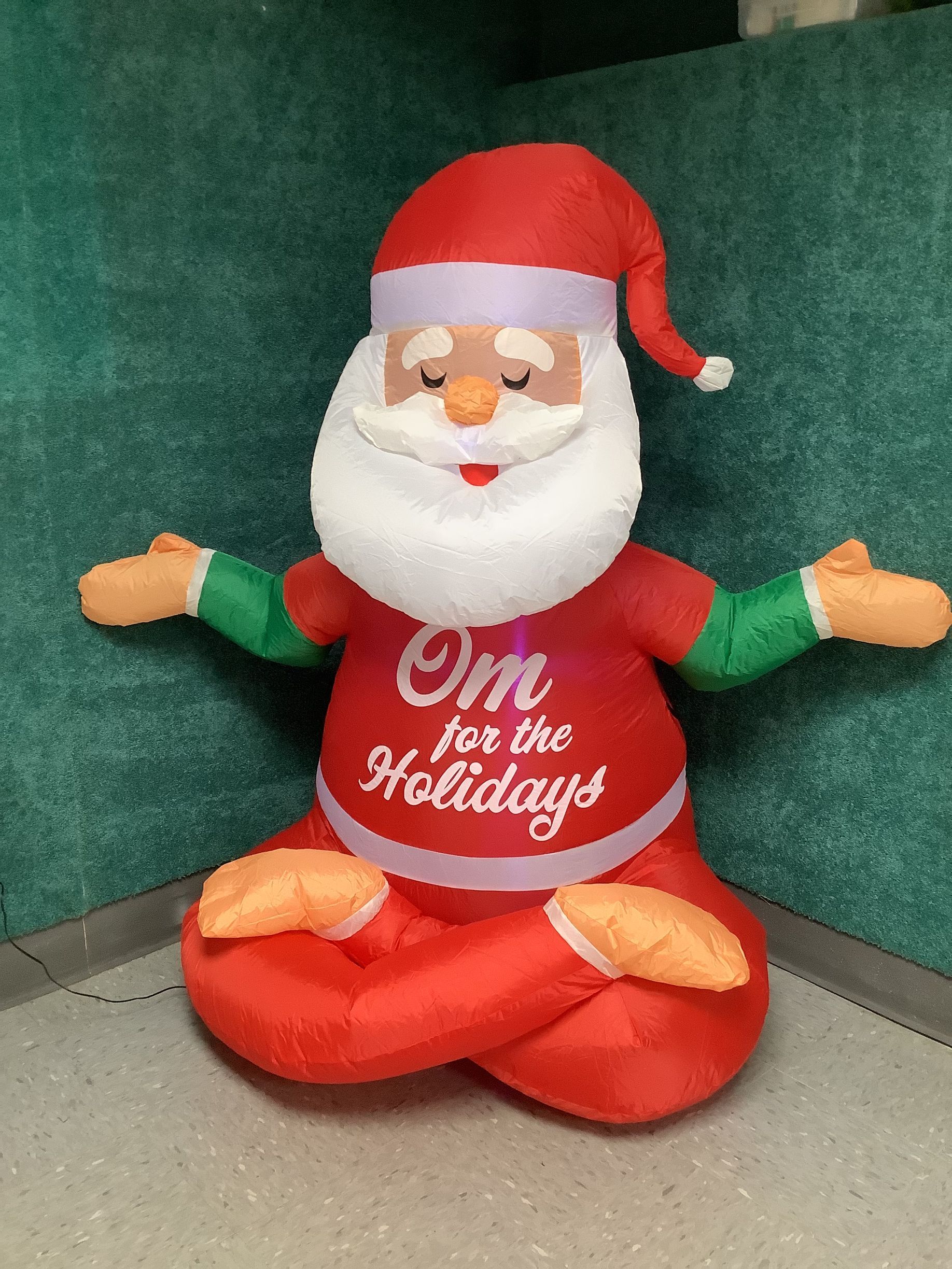 An inflatable santa claus is sitting in a lotus position with his arms outstretched.