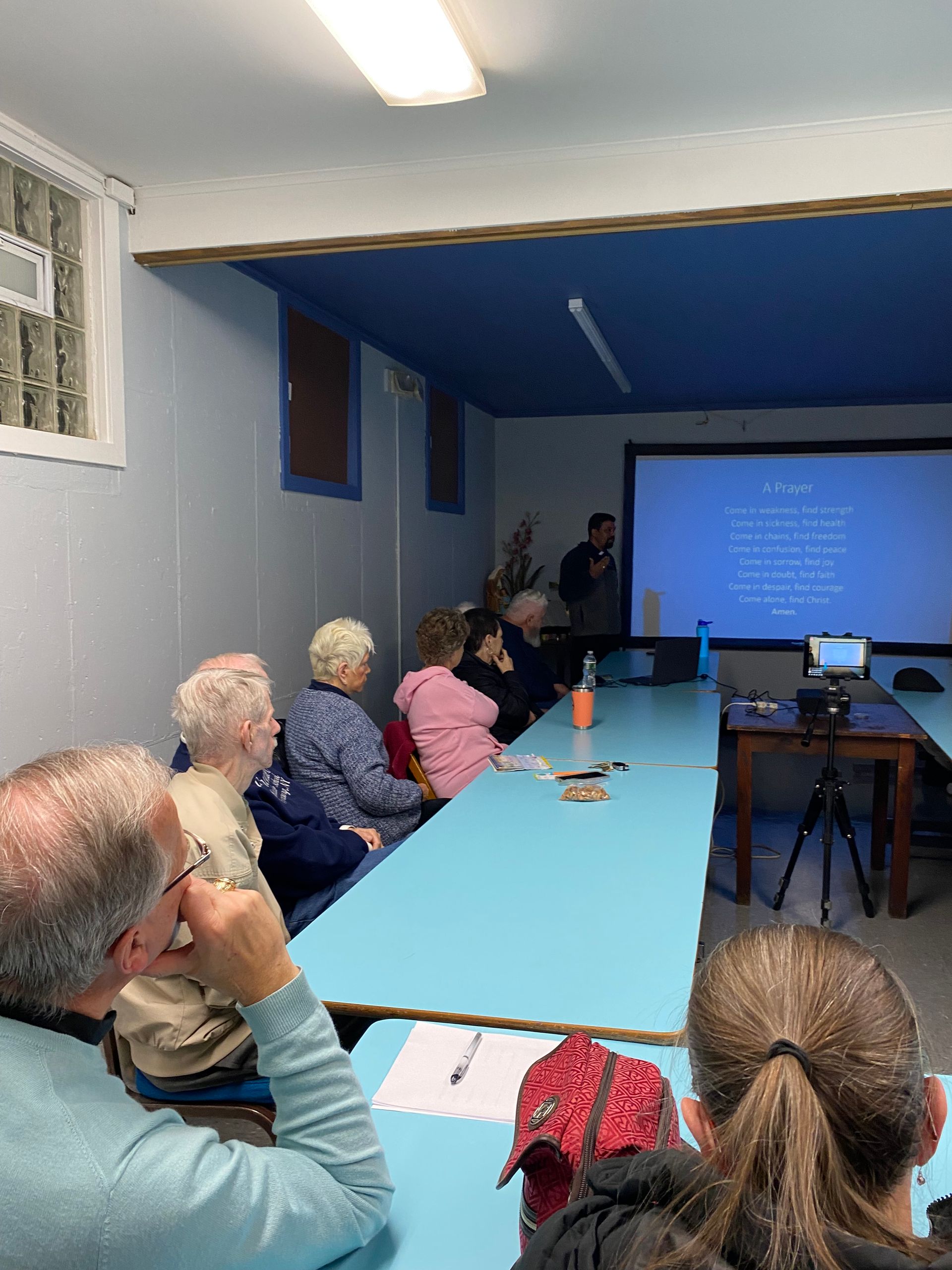 A group of people are sitting at tables in a room watching a presentation.