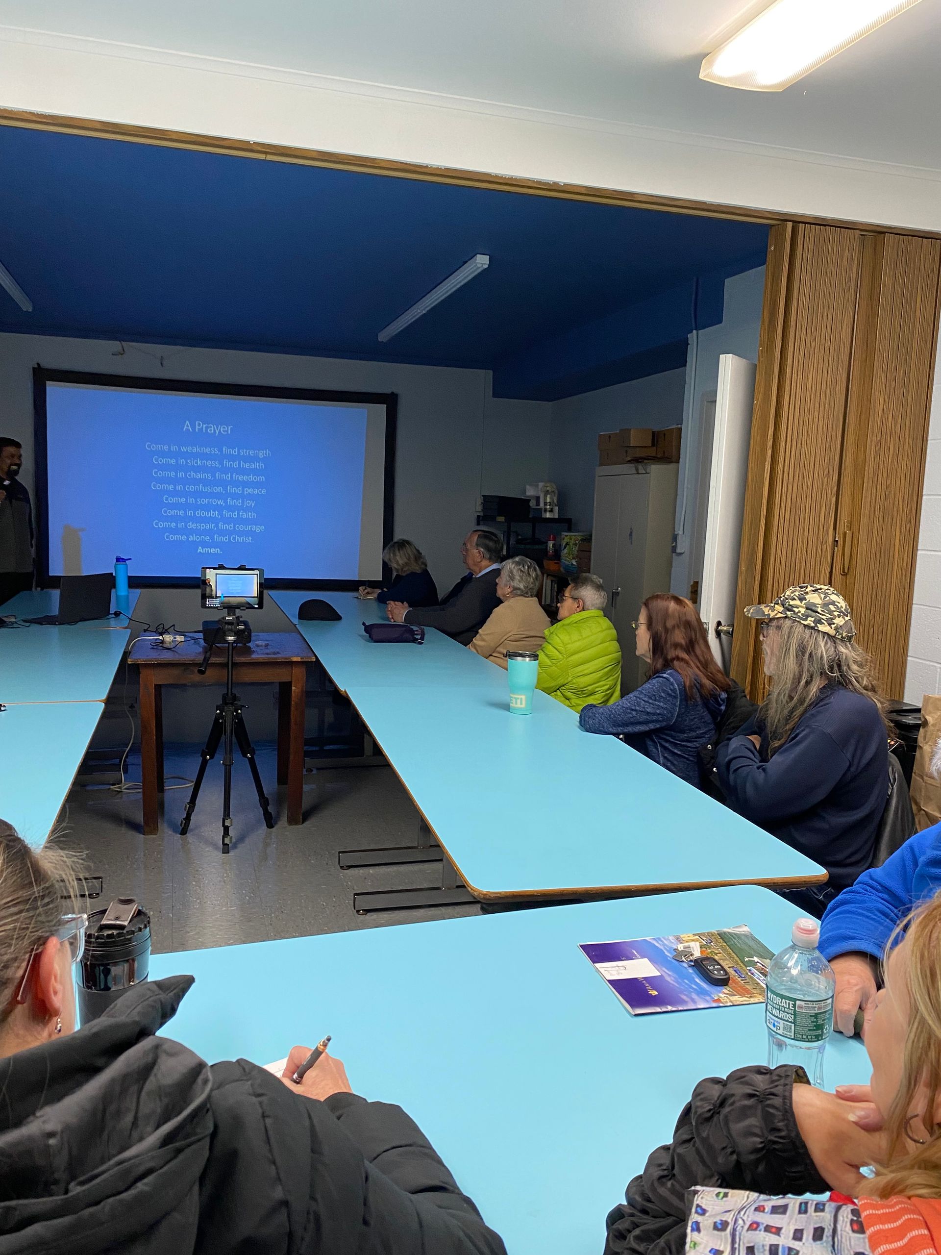 A group of people are sitting at tables in a room watching a presentation.