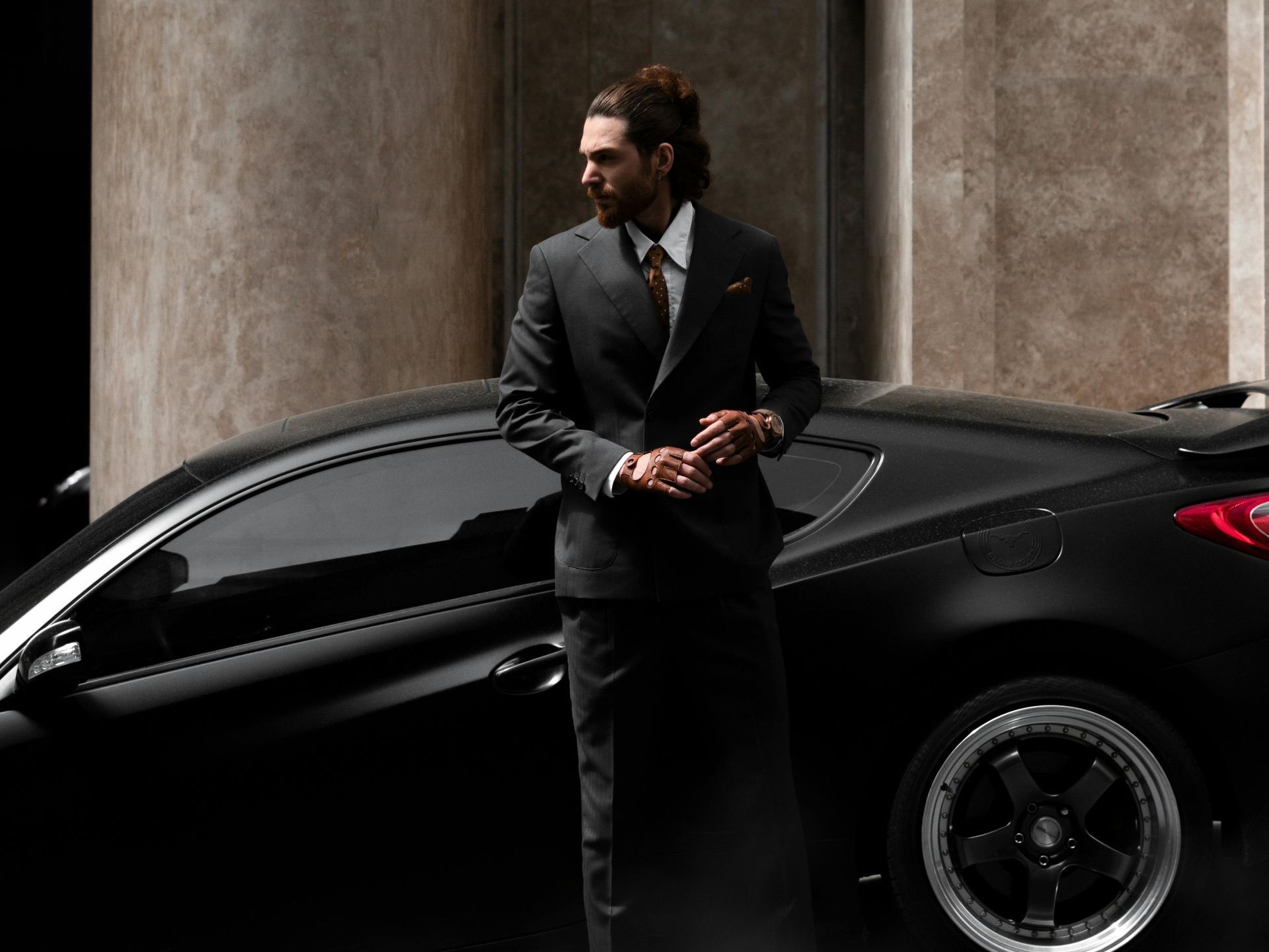 A black car is parked on the side of the road with chauffeur waiting next to it