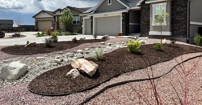 A landscaped front yard with mulch beds, rocks, and a gravel path leading to a house with a gray exterior.
