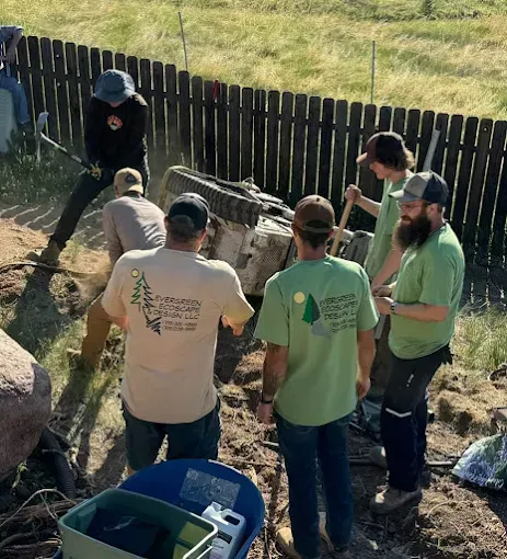 Group of people working on landscaping near a fence, using shovels and other tools.