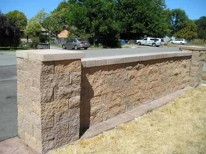 Stone retaining wall bordering a paved area with cars and trees in the background.