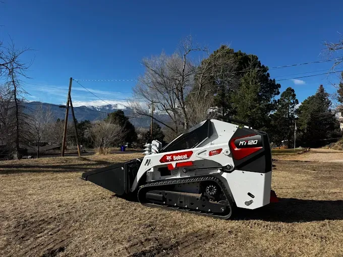 Bobcat M300T skid-steer loader on brown field with mountain backdrop. Clear blue sky.