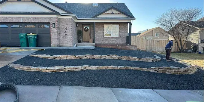 A house with a black gravel landscape, stone borders, and a person working on the yard.