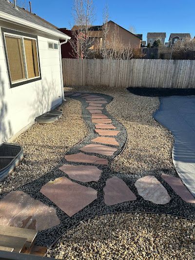 Flagstone path through a backyard with gravel and a fence.