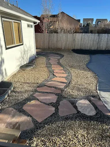 Stone pathway through a gravel yard beside a house and a pool.