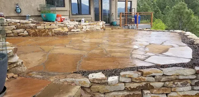 Wet stone patio with retaining wall, overlooking a forested landscape.
