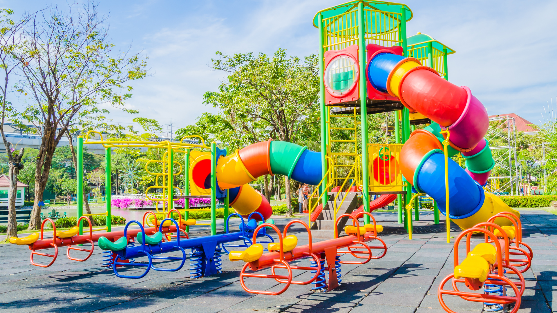 A colorful playground with multi-colored tube slides and several seesaws on a rubber ground surface in a park.