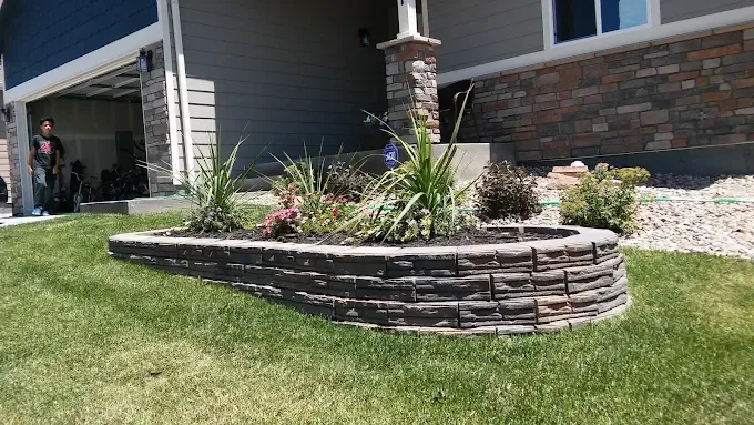 Raised flower bed with stone blocks, filled with plants, in front of a house.