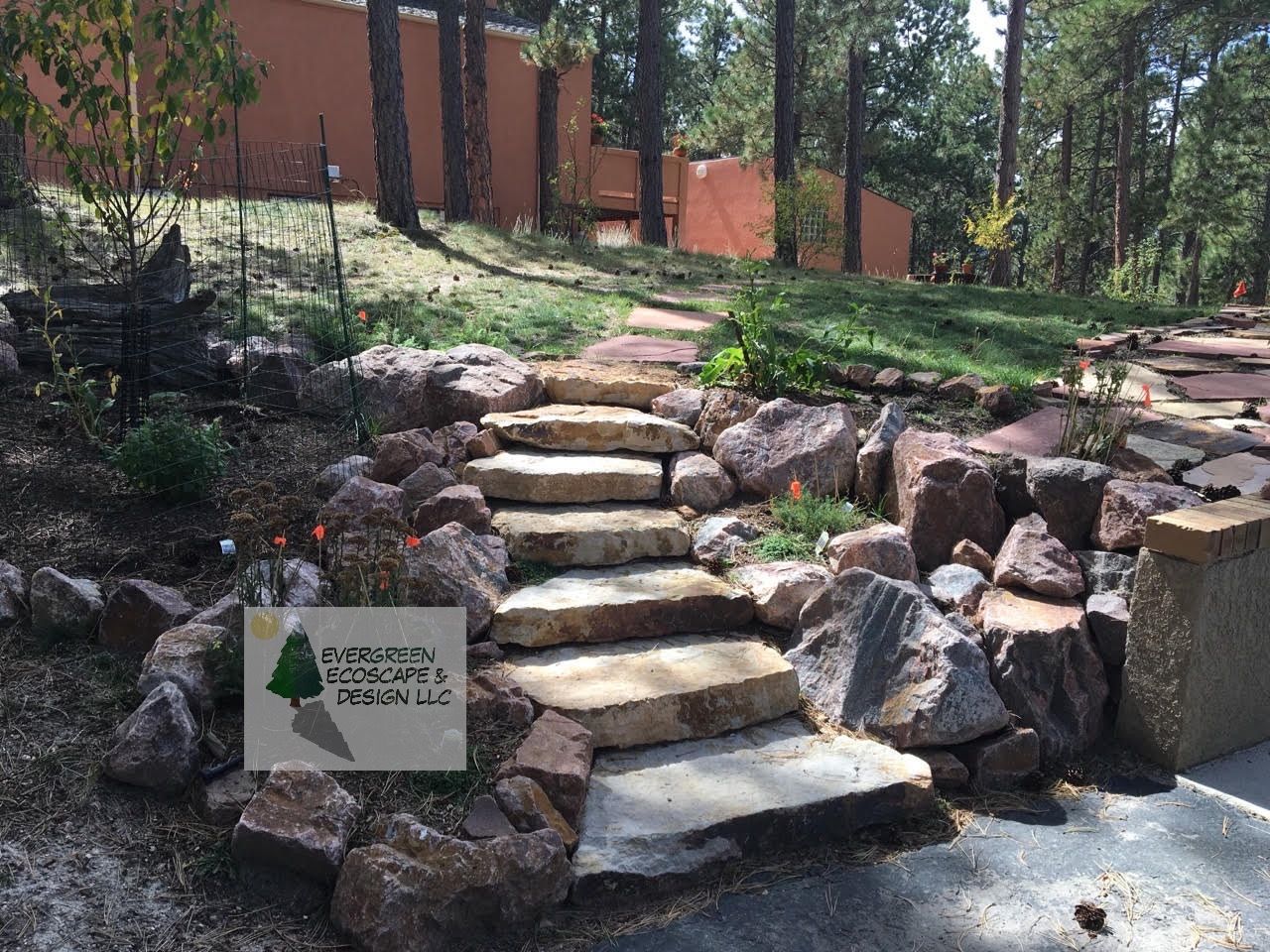 Wooden Adirondack chair on stone patio next to a rock-lined pond.